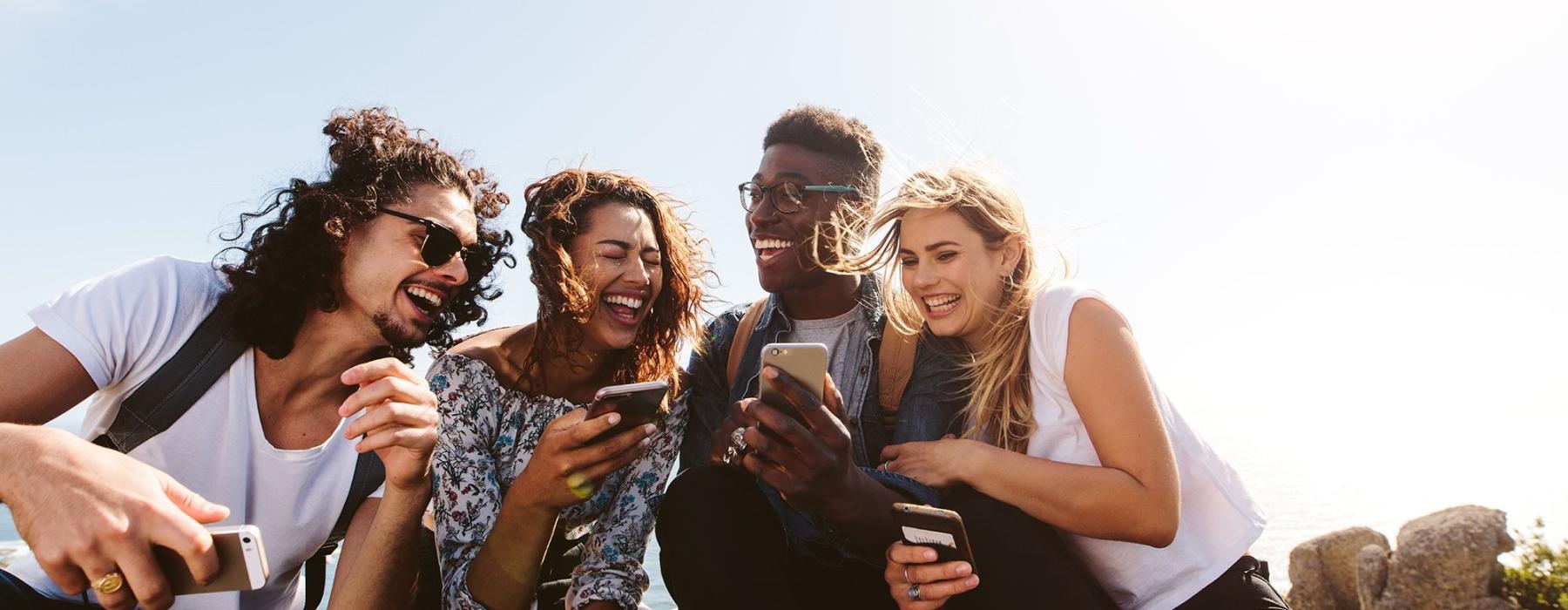 a group of friends sit outside laughing over their cell phones