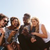 a group of friends sit outside laughing over their cell phones